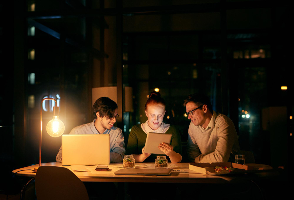Three colleagues around one screen in the evening, looking at the same work